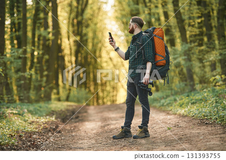 Smartphone in hand. Bearded man is in the forest at daytime Smartphone in hand. Bearded man is in the forest at daytime 131393755