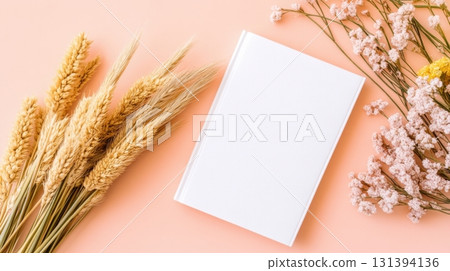 Mockup of a blank white book cover surrounded by dried flowers against a peach-colored background highlighting simplicity and elegance 131394136