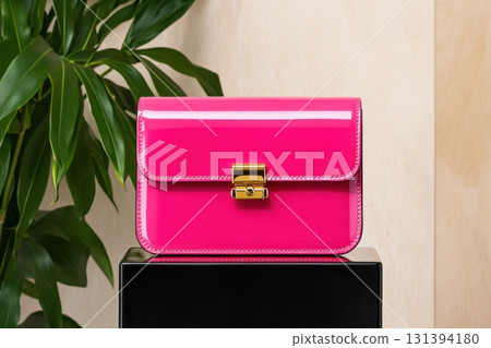 Stylish tiny rectangular clutch in glossy patent leather with vibrant pink color and gold hardware displayed on sleek black pedestal 131394180