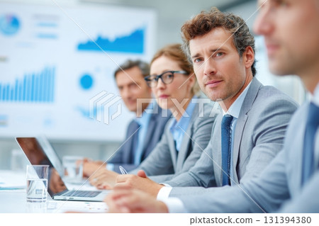 Business meeting with diverse professionals in grey suits, discussing strategies and analyzing data on charts, showcasing teamwork and collaboration in a modern office environment 131394380