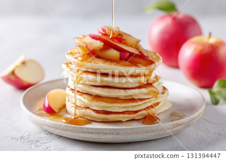 Stack of fluffy pancakes topped with caramel and fresh apple slices, served on a rustic plate, creating a delicious breakfast scene with inviting textures and colors 131394447