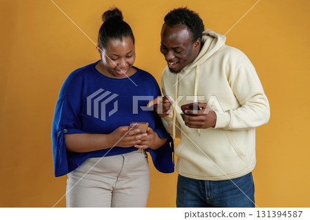 Using smartphones. Happy black couple are together against yellow background Using smartphones. Happy black couple are together against yellow background 131394587