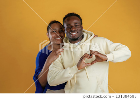 Showing love gesture. Happy black couple are together against yellow background Showing love gesture. Happy black couple are together against yellow background 131394593