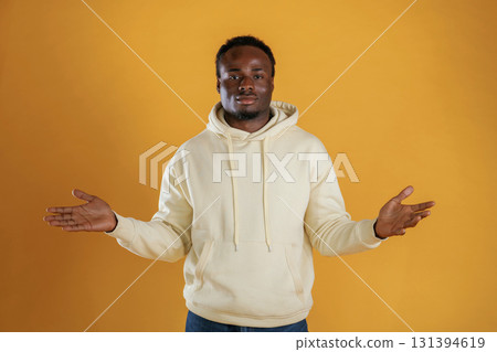 Cheerful black guy is against yellow background with opened arms Cheerful black guy is against yellow background with opened arms 131394619