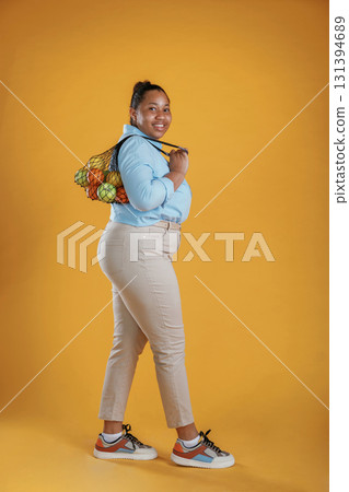 Bunch of fruits in the bag, holding. African American woman is in the studio against yellow background 131394689