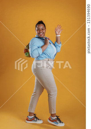 Bunch of fruits in the bag, holding. African American woman is in the studio against yellow background 131394690