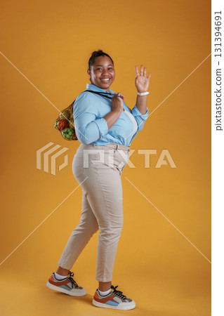 Bunch of fruits in the bag, holding. African American woman is in the studio against yellow background 131394691