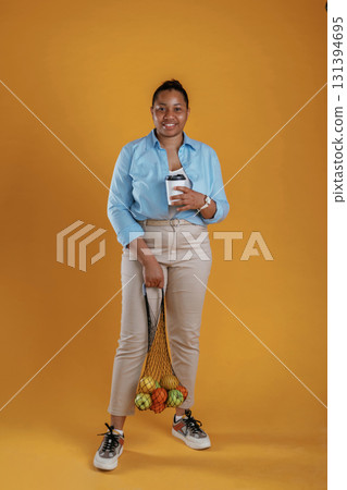 Fresh coffee. Customer with bunch of fruits in the bag, holding. African American woman is in the studio 131394695