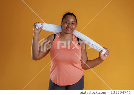 With white towel, after exercise. African American woman is in the studio against yellow background With white towel, after exercise. African American woman is in the studio against yellow background 131394745