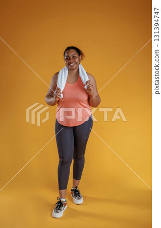 With white towel, after exercise. African American woman is in the studio against yellow background 131394747