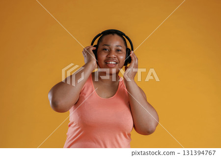 Front view, in headphones, listening to music. African American woman is in the studio against yellow background 131394767