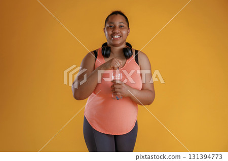 Bottle of water, break, standing with headphones on the neck. African American woman is in the studio Bottle of water, break, standing with headphones on the neck. African American woman is in the studio 131394773
