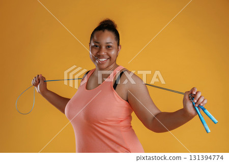 Jumping rope, standing. African American woman is in the studio against yellow background 131394774