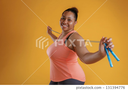 Jumping rope, standing. African American woman is in the studio against yellow background Jumping rope, standing. African American woman is in the studio against yellow background 131394776