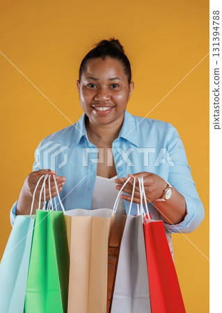 Shopping bags in hands. African American woman is in the studio against yellow background 131394788