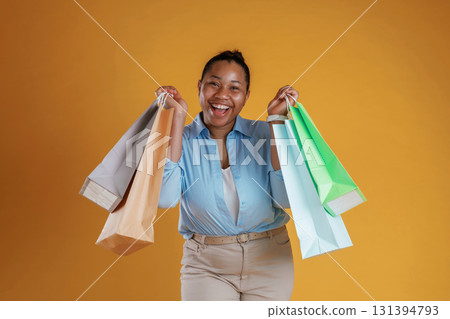 Colorful shopping bags in hands. African American woman is in the studio against yellow background 131394793