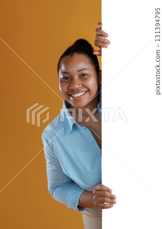 White copy space wall, hiding behind it. African American woman is in the studio against yellow background 131394795