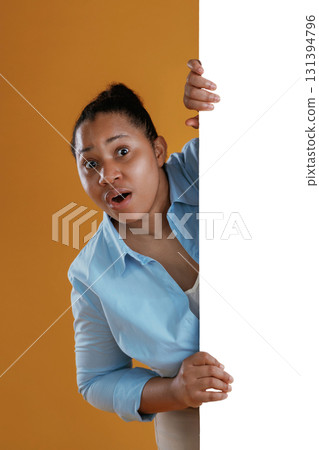 White copy space wall, hiding behind it. African American woman is in the studio against yellow background White copy space wall, hiding behind it. African American woman is in the studio against yellow background 131394796