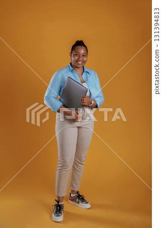 Silver colored modern laptop in hands. African American woman is in the studio against yellow background Silver colored modern laptop in hands. African American woman is in the studio against yellow background 131394813