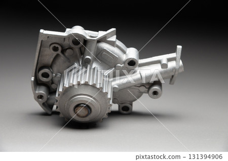 A new, shiny aluminum engine coolant pump on a gray gradient background. Contrast backlighting. A new, shiny aluminum engine coolant pump on a gray gradient background. Contrast backlighting. 131394906
