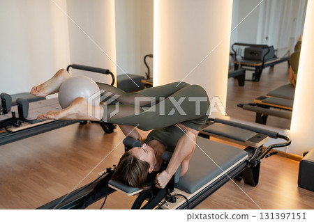 Woman doing Pilates exercise for core and back muscles on Reformer machine with determination and focus on strength body Woman doing Pilates exercise for core and back muscles on Reformer machine with determination and focus on strength body 131397151
