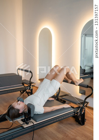 Woman training on the reformer bed at Glute bridge Pilates workout. Reformer pilates studio machine for fitness workouts in gym. Fit, healthy and strong authentical body. Fitness concept 131397157