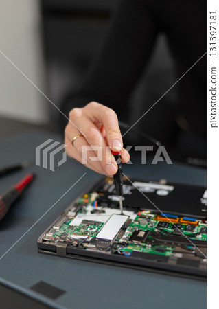Female adult IT technician repairing a laptop motherboard with a precision tool in a workshop 131397181