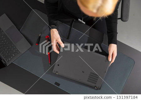 Female IT technician in her 30s repairs laptop at a dark desk with tools nearby 131397184