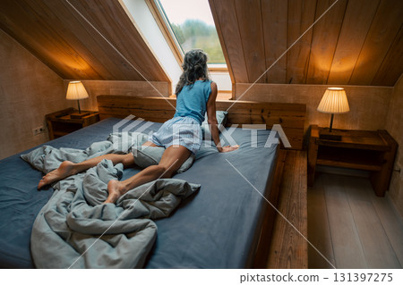 A tranquil bedroom scene with a person gazing thoughtfully out the window, enjoying a cozy atmosphere 131397275