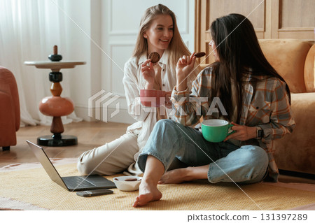 Laptop, cups of tea, sitting and talking. Two happy young female best friends are indoors 131397289