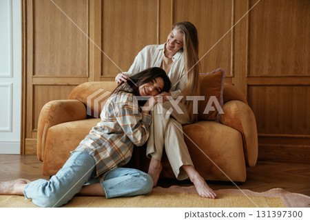 Leaning on the legs of a woman. Two happy young female best friends are indoors Leaning on the legs of a woman. Two happy young female best friends are indoors 131397300