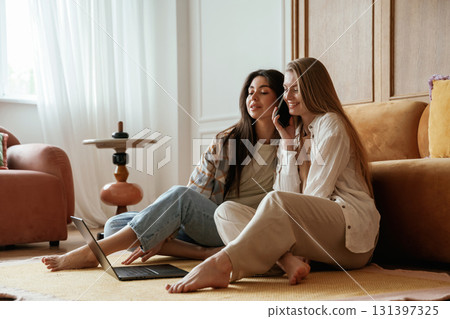 Eavesdrops on what saying on the phone. Two happy young female best friends are indoors 131397325