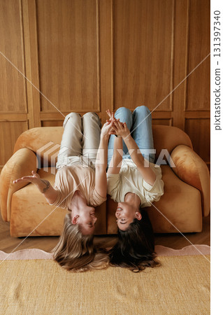 Lying upside down on the sofa with heads down. Two happy young female best friends are indoors Lying upside down on the sofa with heads down. Two happy young female best friends are indoors 131397340