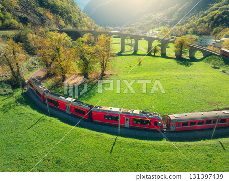Aerial view of red train on spiral viaduct in mountains at sunset Aerial view of red train on spiral viaduct in mountains at sunset 131397439