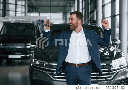 Keys in hand, smiling. A businessman is in a car dealership Keys in hand, smiling. A businessman is in a car dealership 131397462