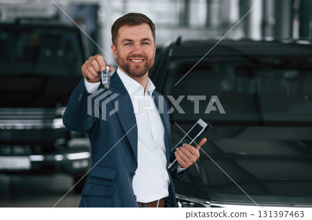 Keys in hand, smiling. A businessman is in a car dealership Keys in hand, smiling. A businessman is in a car dealership 131397463