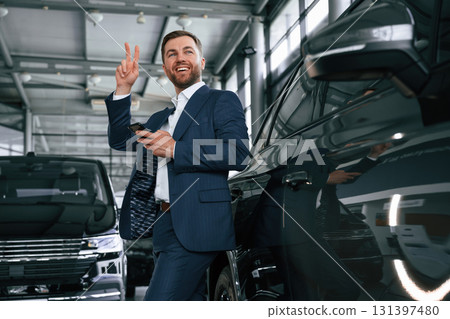 Peace hand gesture. A businessman is in a car dealership Peace hand gesture. A businessman is in a car dealership 131397480