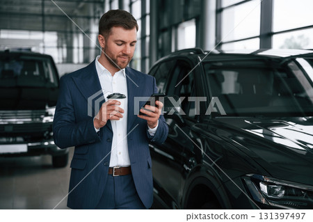 Break, with coffee and smartphone. A businessman is in a car dealership 131397497