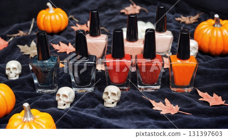 A collection of nail polish bottles featuring fall colors arranged on a dark surface, surrounded by small pumpkins, autumn leaves, and skull decorations, perfect for Halloween. 131397603