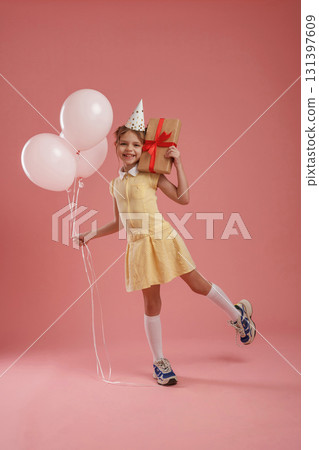Happy, holding gift box and balloons, birthday. Cute little girl is against pink background Happy, holding gift box and balloons, birthday. Cute little girl is against pink background 131397609