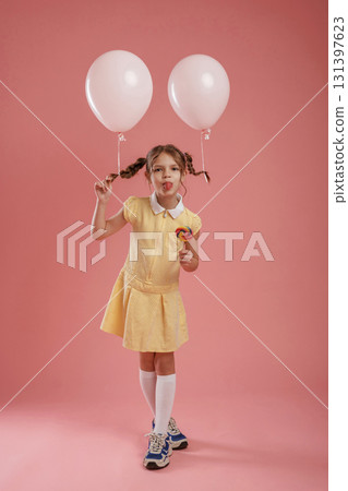 Showing tongue, playful, with balloons. Cute little girl is against pink background 131397623
