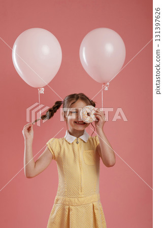 Donut in hand. Cute little girl is against pink background Donut in hand. Cute little girl is against pink background 131397626