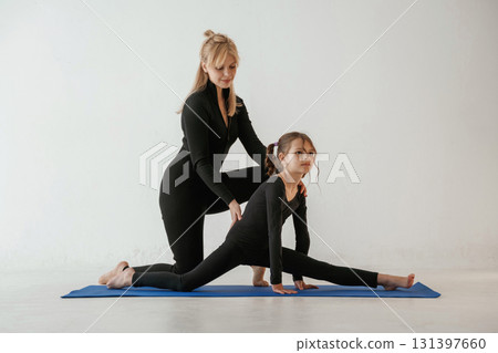 Teaching how to sit on twine. Mother and little daughter are in fitness clothes on yoga mat Teaching how to sit on twine. Mother and little daughter are in fitness clothes on yoga mat 131397660