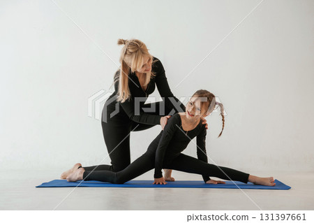 Teaching how to sit on twine. Mother and little daughter are in fitness clothes on yoga mat Teaching how to sit on twine. Mother and little daughter are in fitness clothes on yoga mat 131397661
