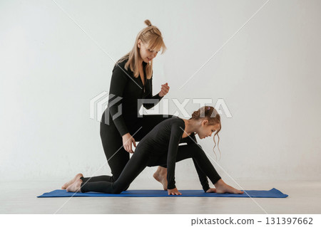 Teaching how to sit on twine. Mother and little daughter are in fitness clothes on yoga mat Teaching how to sit on twine. Mother and little daughter are in fitness clothes on yoga mat 131397662