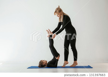 Raising legs up, helping. Mother and little daughter are in fitness clothes on yoga mat Raising legs up, helping. Mother and little daughter are in fitness clothes on yoga mat 131397663