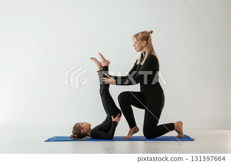Raising legs up, helping. Mother and little daughter are in fitness clothes on yoga mat Raising legs up, helping. Mother and little daughter are in fitness clothes on yoga mat 131397664