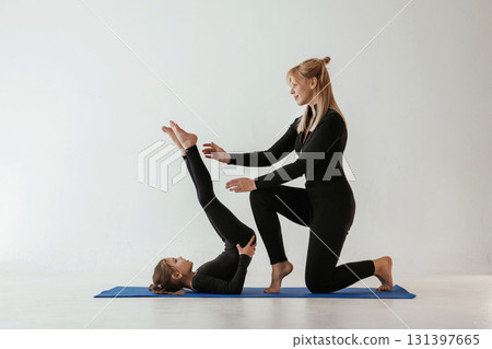 Raising legs up, helping. Mother and little daughter are in fitness clothes on yoga mat Raising legs up, helping. Mother and little daughter are in fitness clothes on yoga mat 131397665
