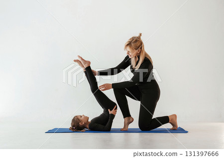 Raising legs up, helping. Mother and little daughter are in fitness clothes on yoga mat Raising legs up, helping. Mother and little daughter are in fitness clothes on yoga mat 131397666