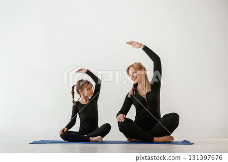 Warm up exercises for hands and spine. Mother and little daughter are in fitness clothes on yoga mat 131397676